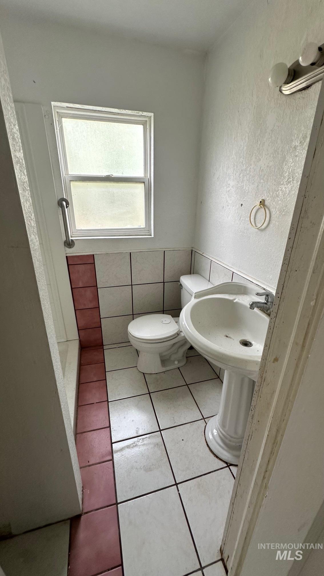 Bathroom featuring light tile patterned floors, a textured wall, tile walls, and a stall shower