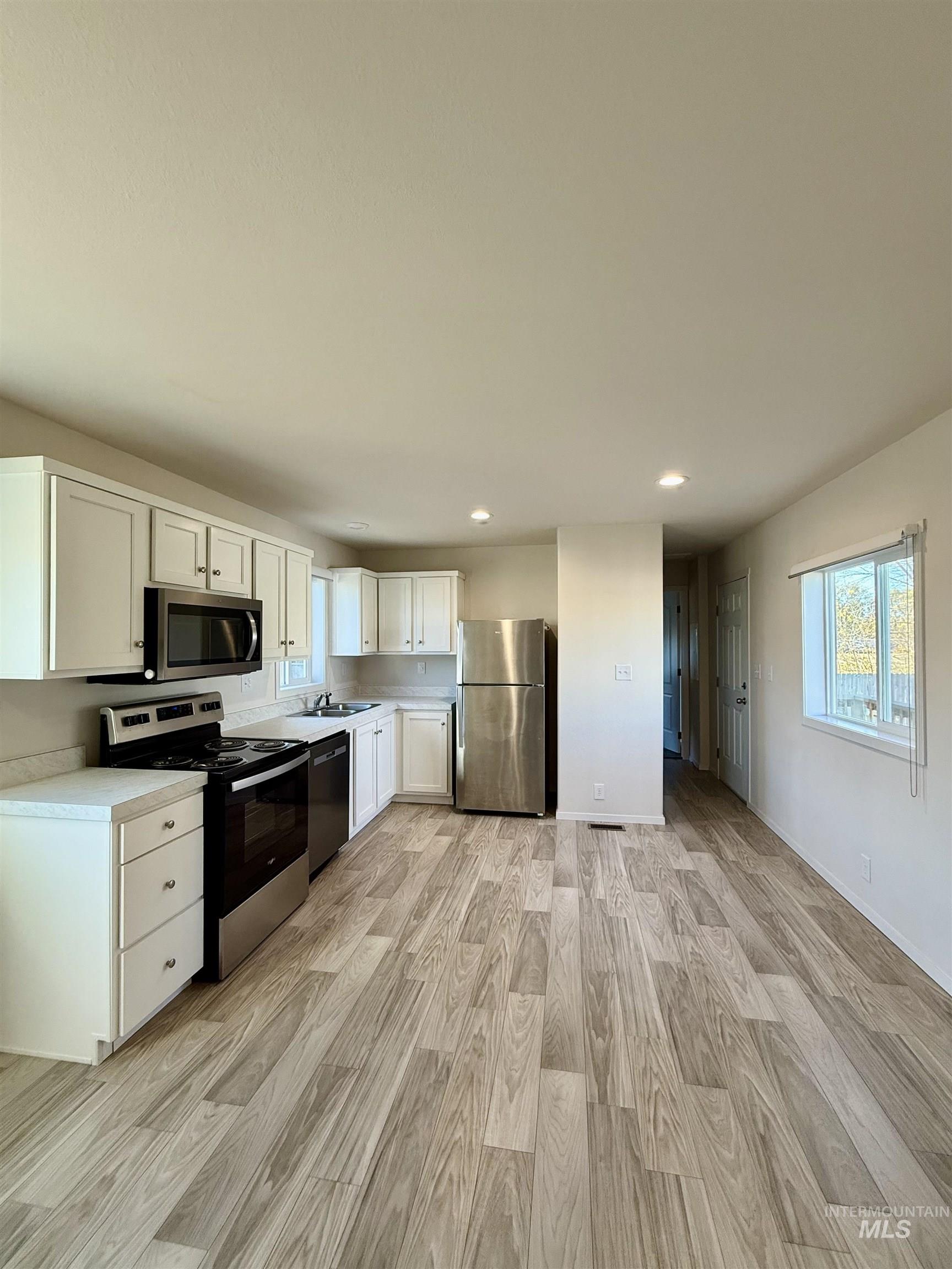 Kitchen featuring white cabinets, appliances with stainless steel finishes, light countertops, light wood-style floors, and recessed lighting
