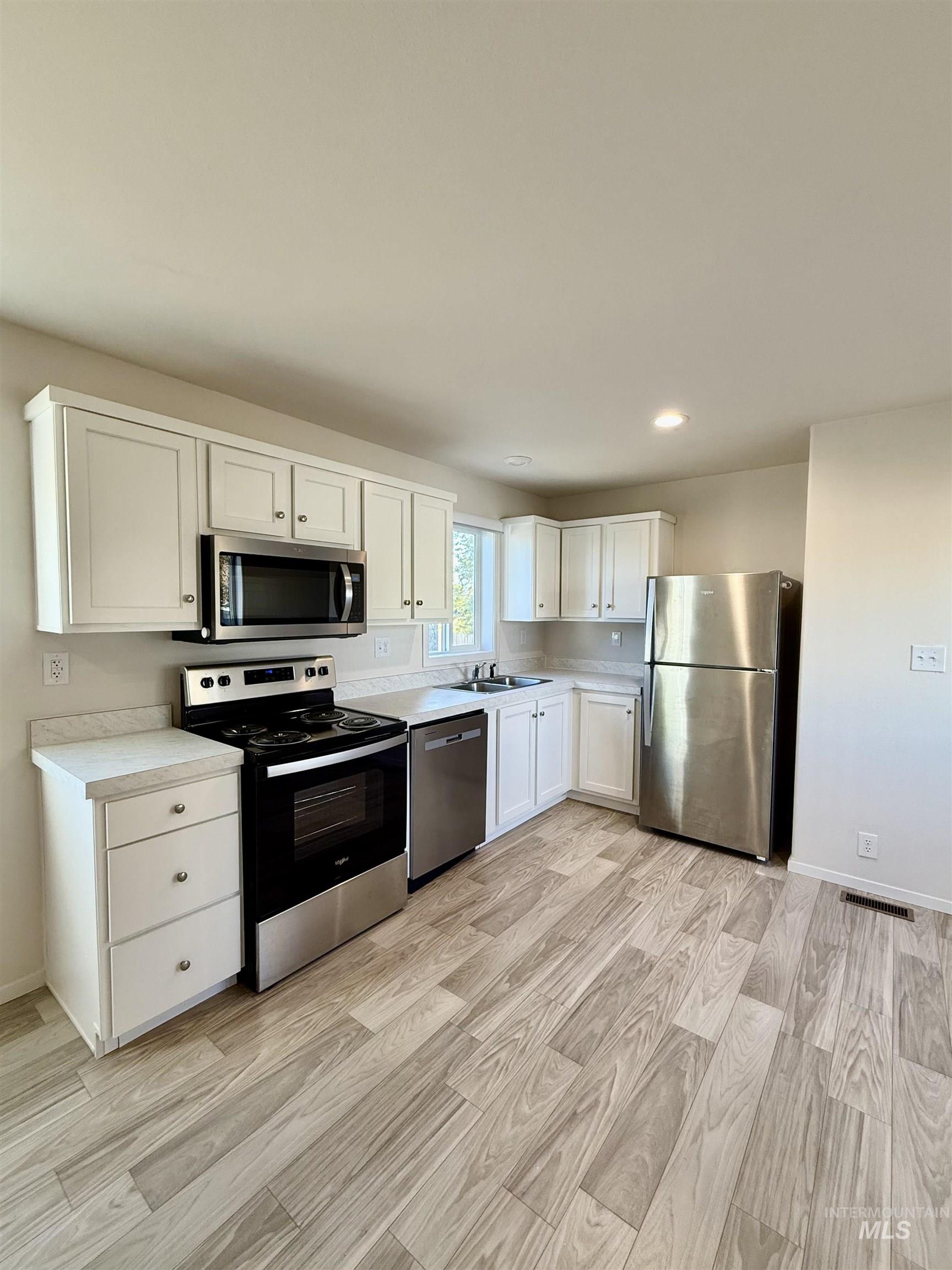 Kitchen with stainless steel appliances, white cabinetry, light countertops, light wood-style flooring, and recessed lighting