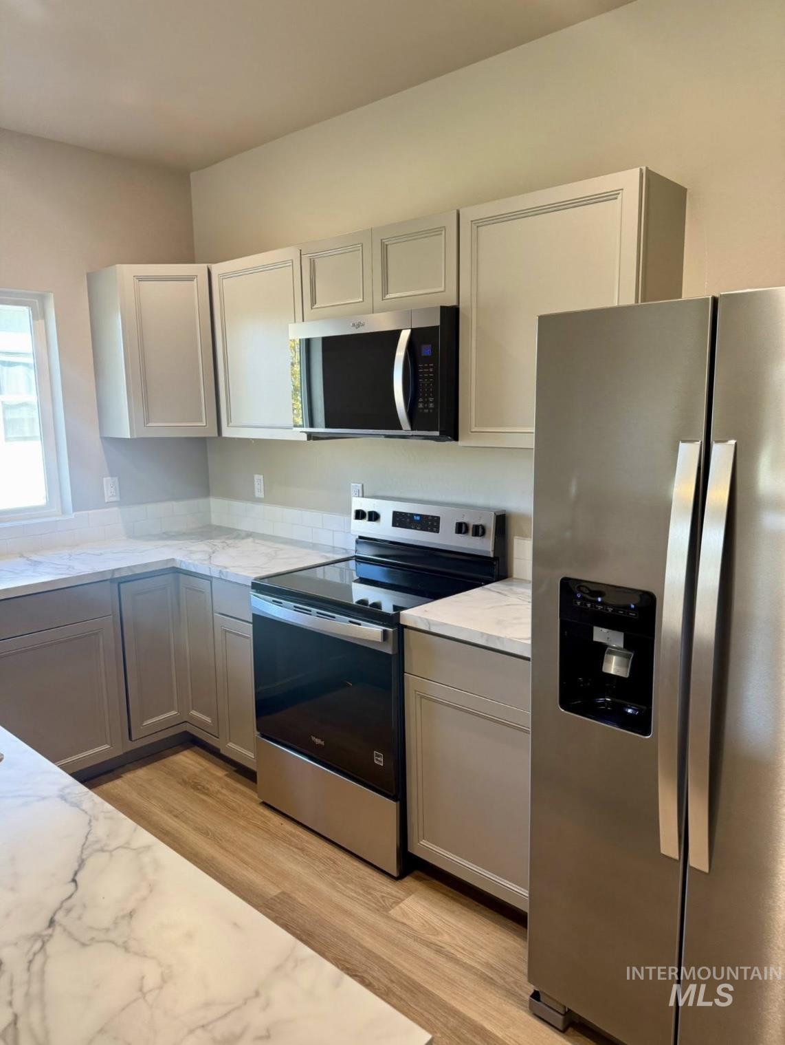 Kitchen featuring appliances with stainless steel finishes, gray cabinets, light wood-style floors, and light stone counters