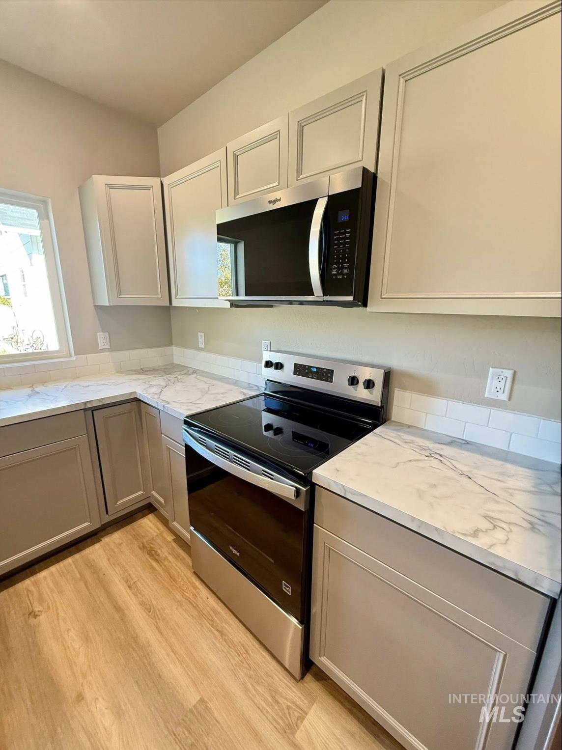 Kitchen with stainless steel appliances, light wood-style floors, and gray cabinetry