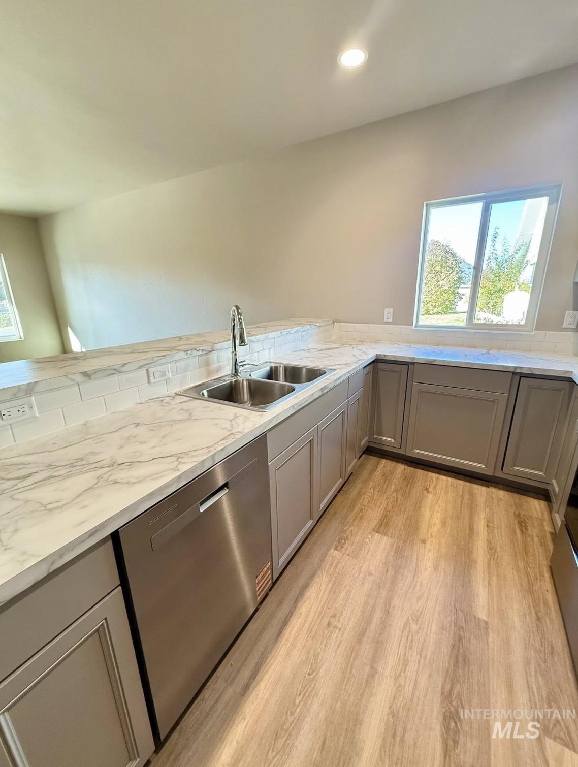 Kitchen with gray cabinets, light wood finished floors, dishwasher, light stone countertops, and recessed lighting