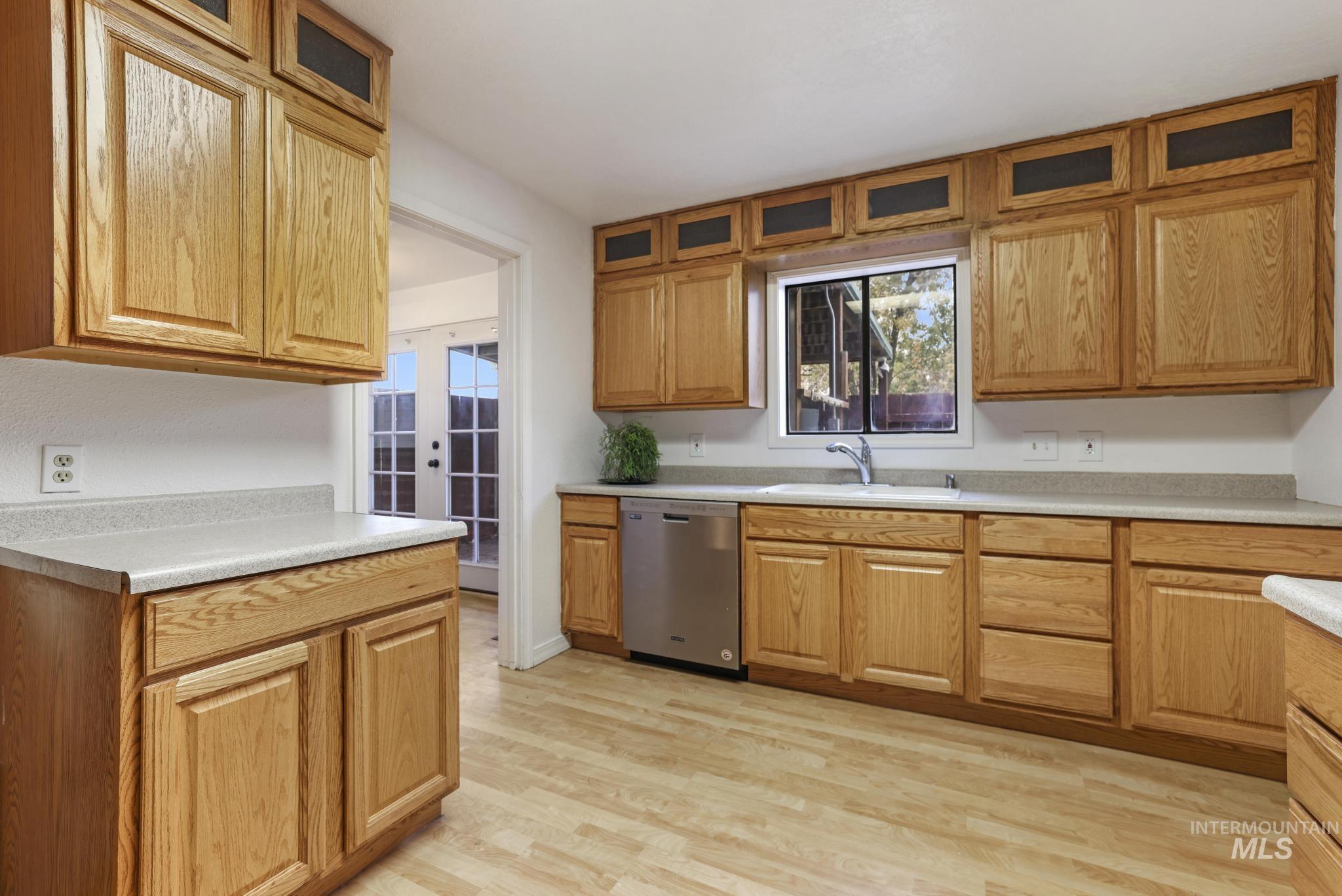Kitchen featuring glass insert cabinets, light countertops, stainless steel dishwasher, and light wood-type flooring