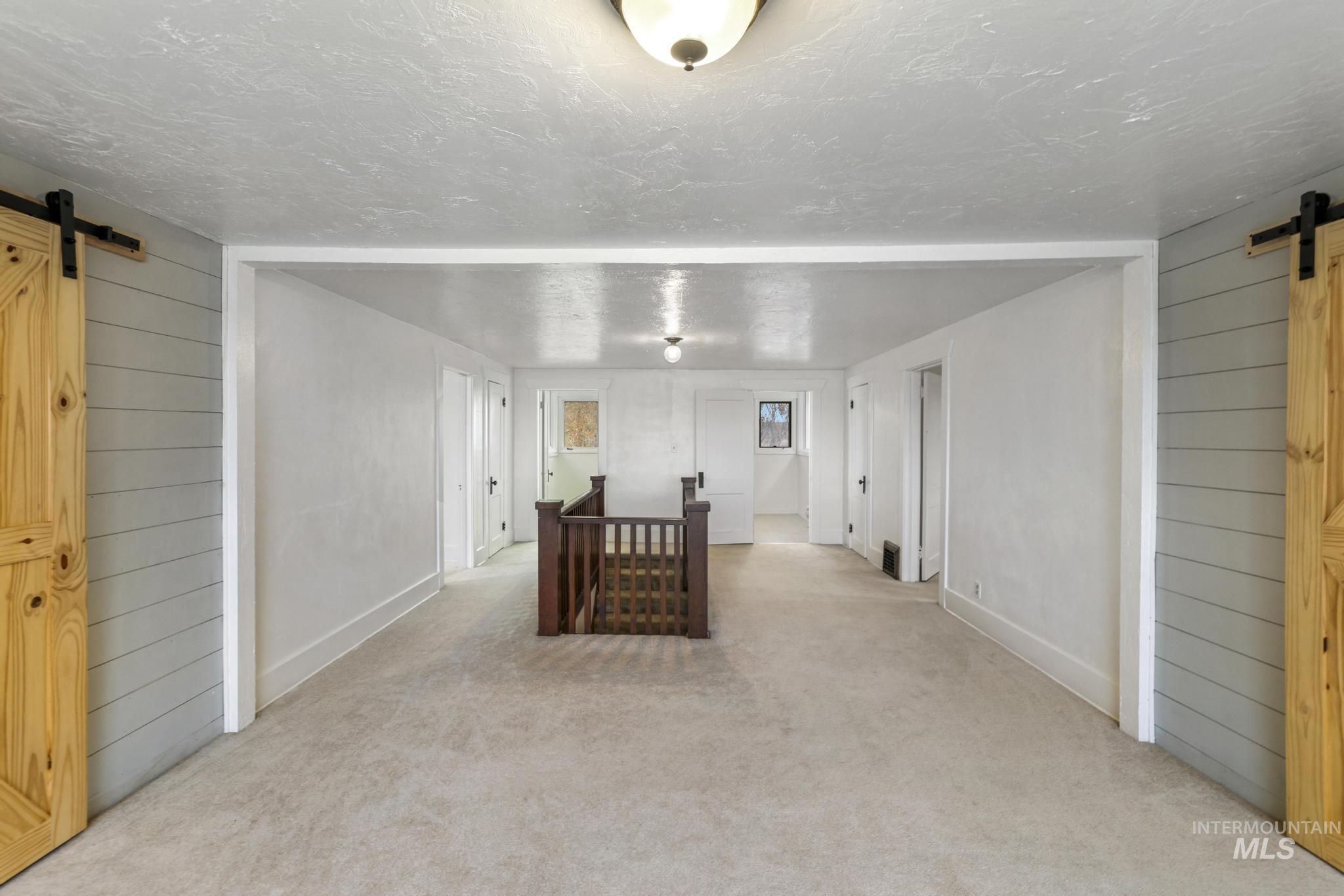 Unfurnished room featuring a barn door, wooden walls, carpet floors, and a textured ceiling
