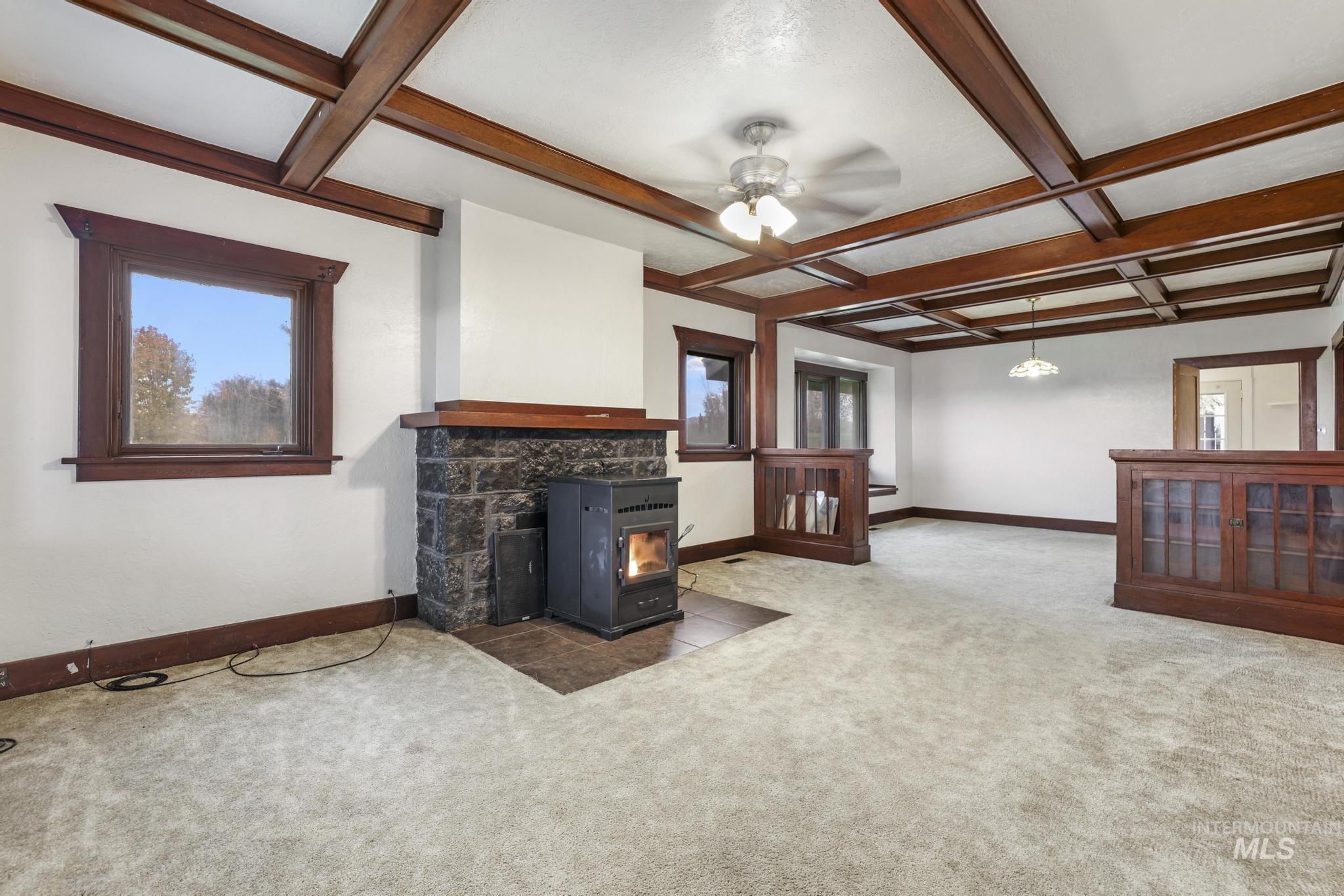 Unfurnished living room with coffered ceiling, beam ceiling, carpet floors, a wood stove, and ceiling fan