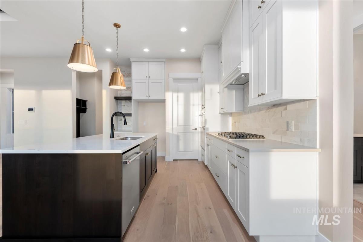 Kitchen featuring white cabinets, light wood-style floors, an island with sink, hanging light fixtures, and recessed lighting