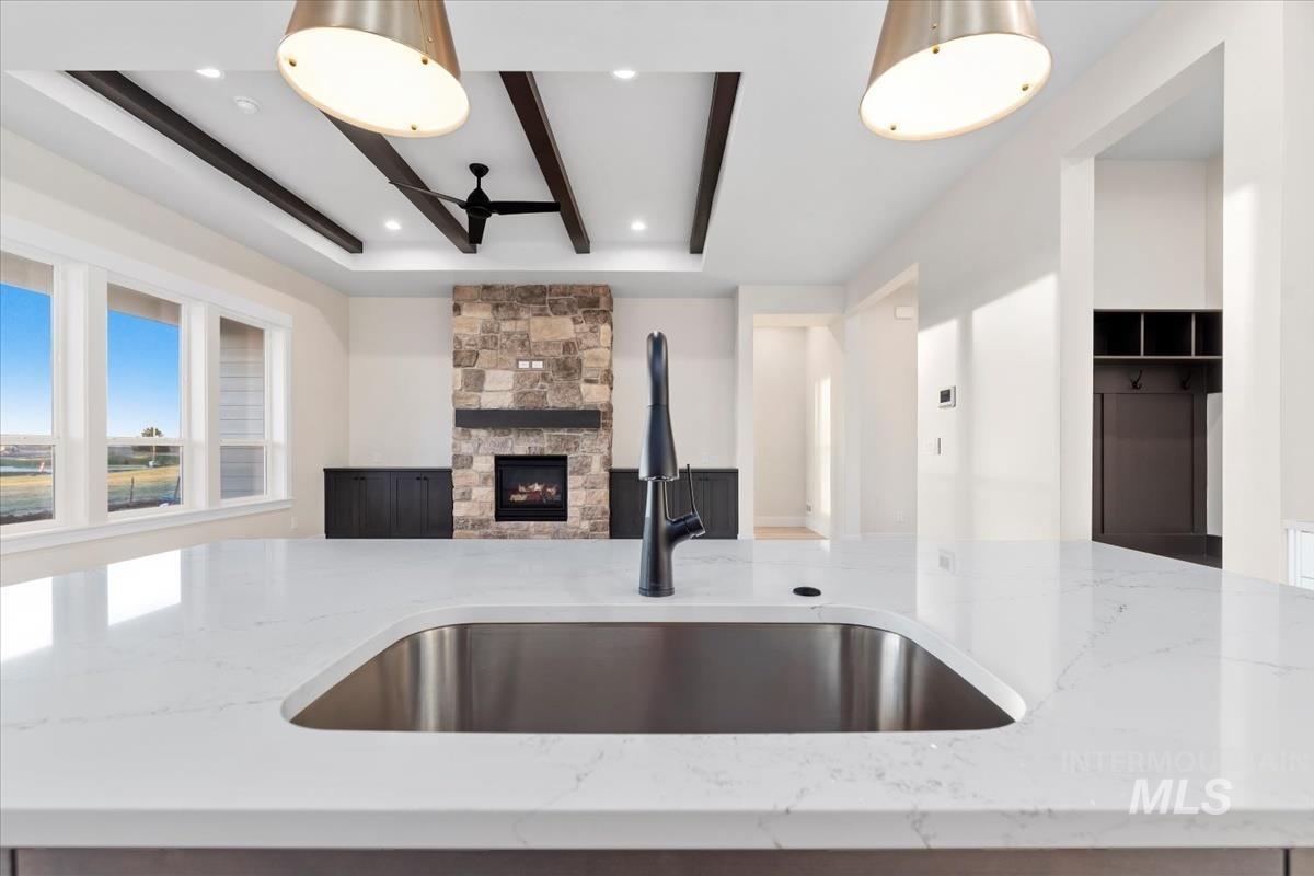 Kitchen with beam ceiling, light stone counters, a stone fireplace, and a ceiling fan