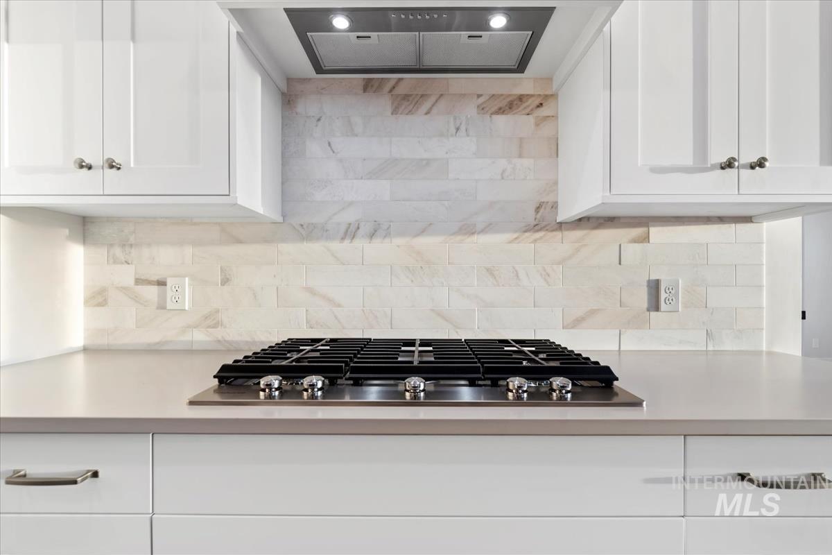 Kitchen featuring white cabinets, ventilation hood, stainless steel gas stovetop, and backsplash