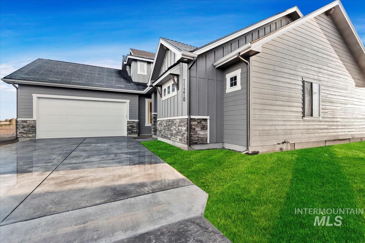 View of front facade with board and batten siding, stone siding, a front yard, and concrete driveway
