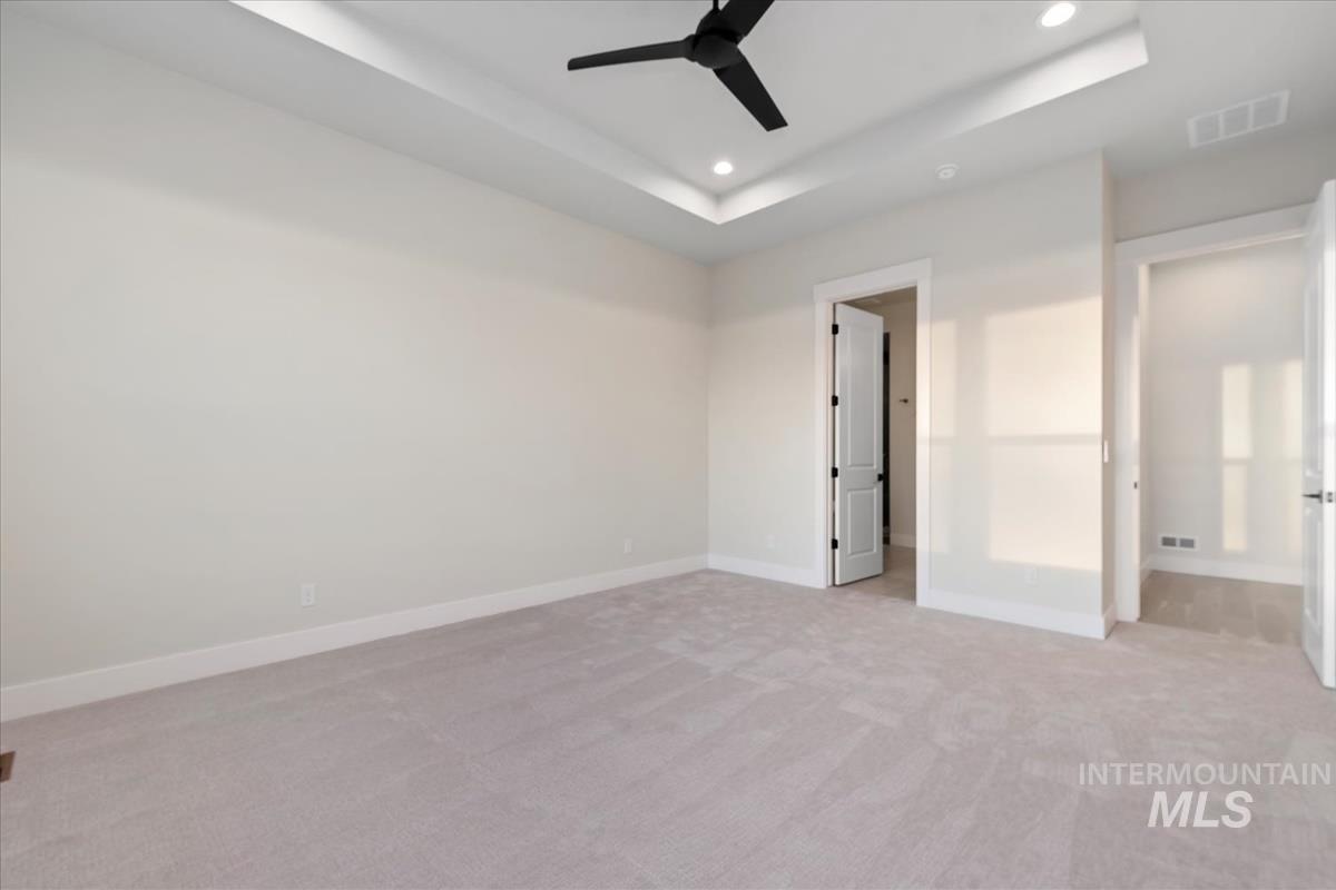 Unfurnished bedroom with a tray ceiling, light colored carpet, ceiling fan, and recessed lighting