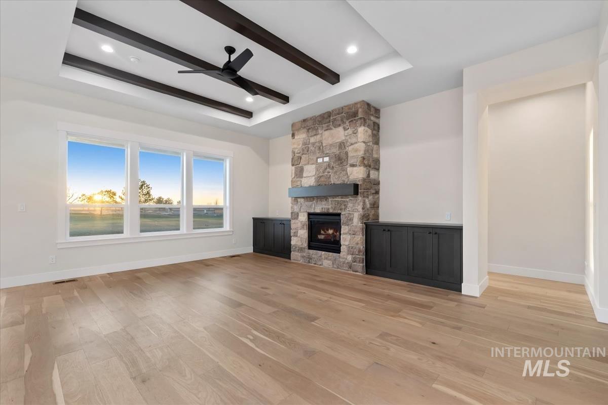 Unfurnished living room with beam ceiling, a fireplace, a raised ceiling, light wood-style floors, and a ceiling fan