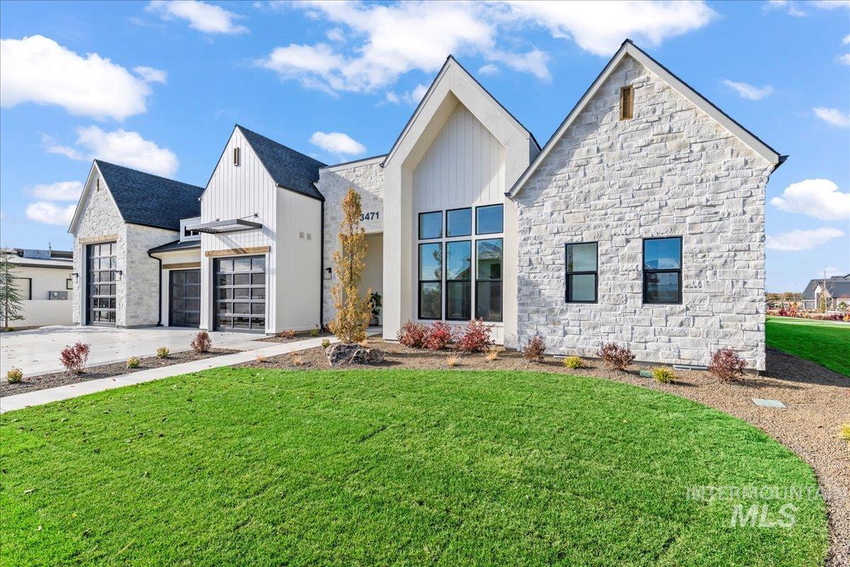 View of front of property with a front yard, board and batten siding, stone siding, concrete driveway, and an attached garage
