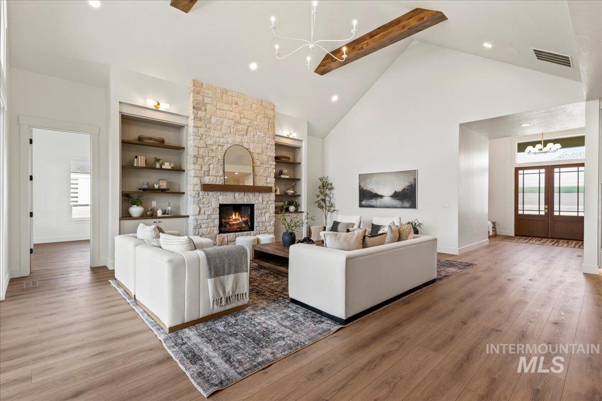 Living area with a chandelier, plenty of natural light, high vaulted ceiling, light wood finished floors, and beam ceiling