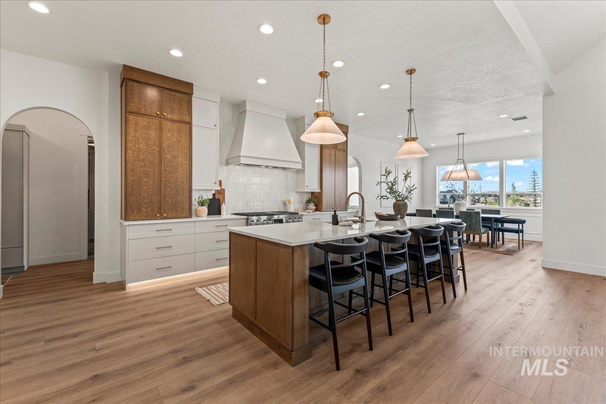 Kitchen featuring arched walkways, brown cabinets, white cabinets, a breakfast bar area, and recessed lighting