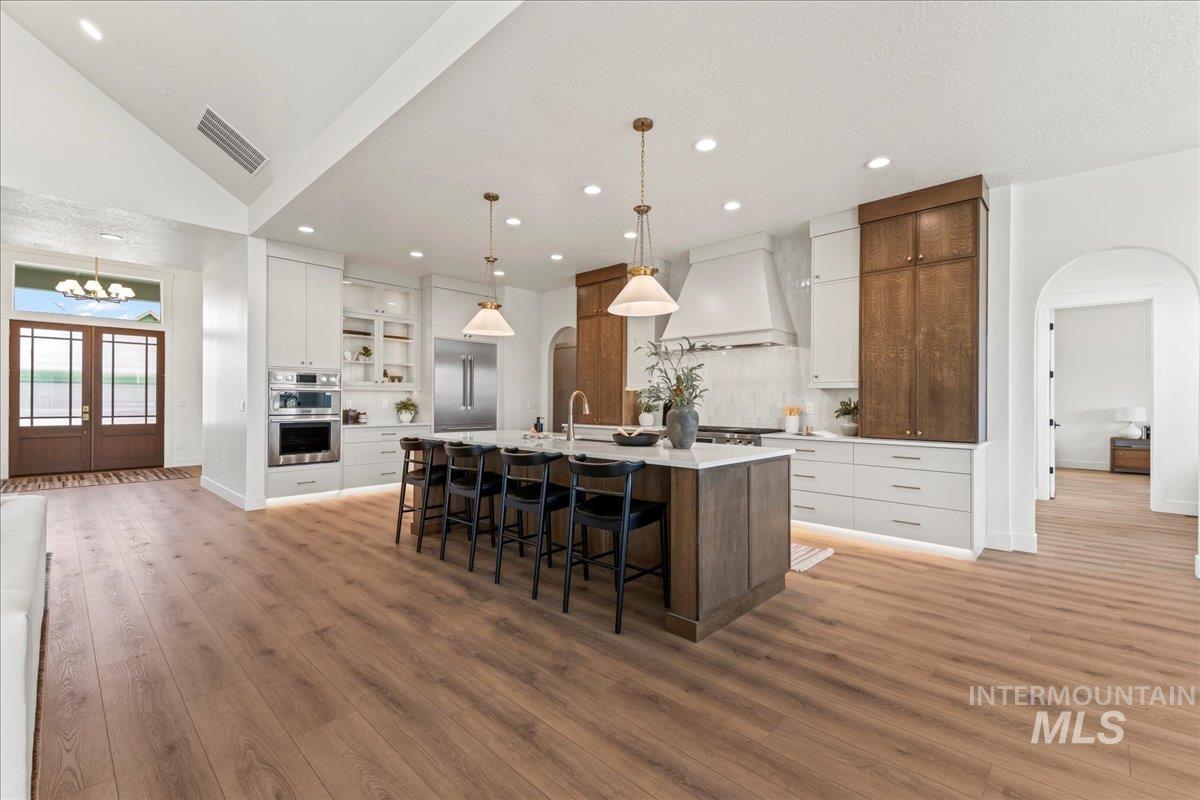 Kitchen featuring white cabinetry, arched walkways, a center island with sink, a kitchen bar, and recessed lighting