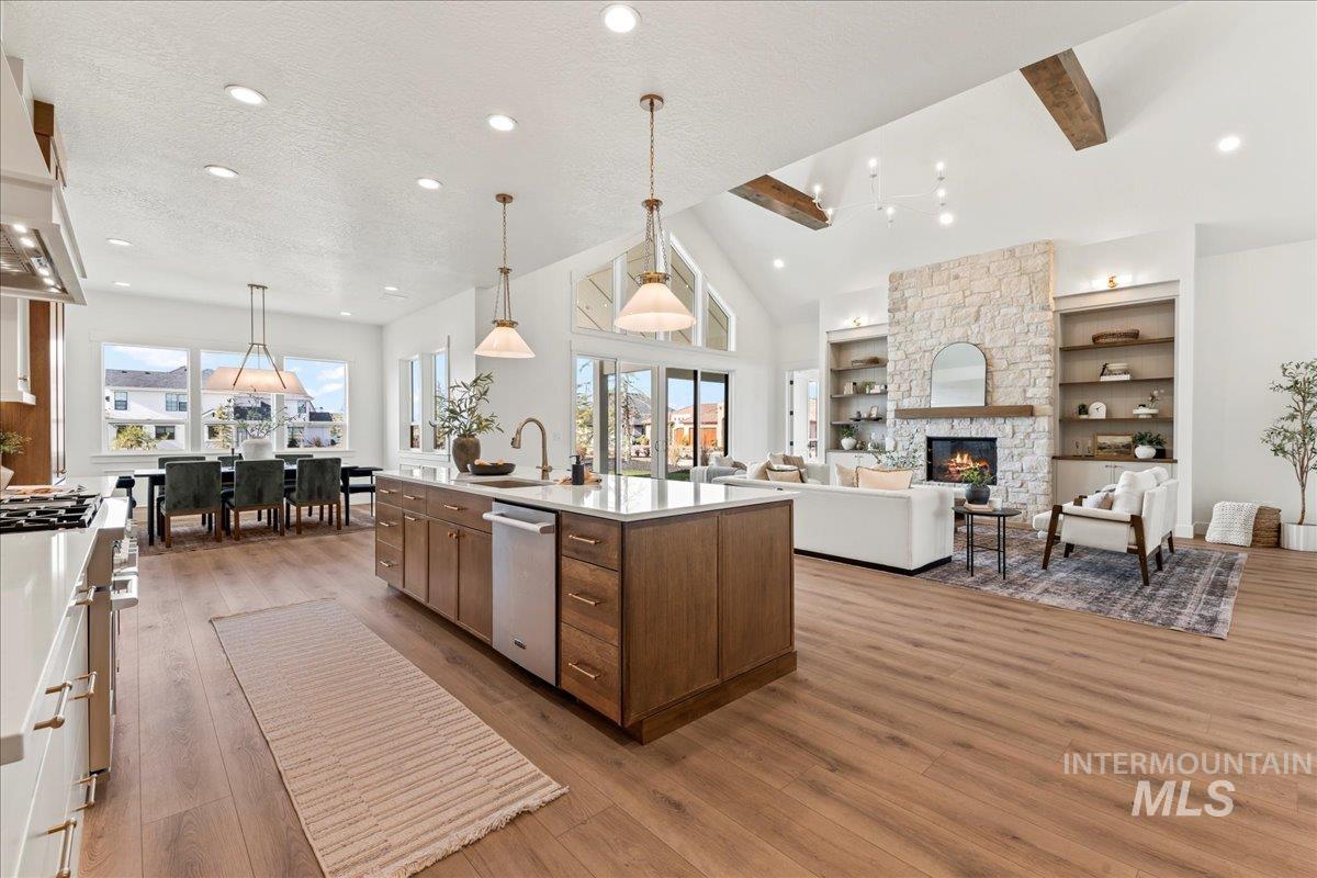 Kitchen featuring hanging light fixtures, open floor plan, a fireplace, a center island with sink, and beamed ceiling