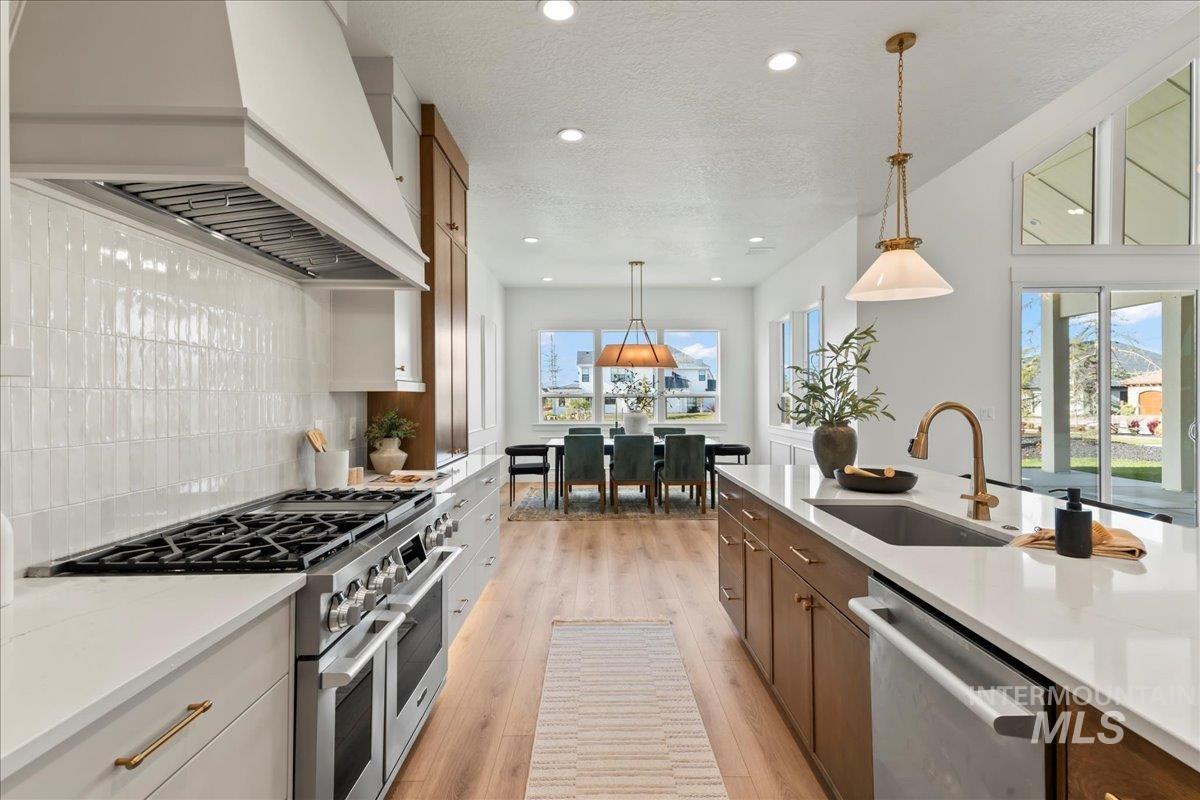 Kitchen with stainless steel appliances, custom range hood, decorative light fixtures, light wood-style flooring, and recessed lighting