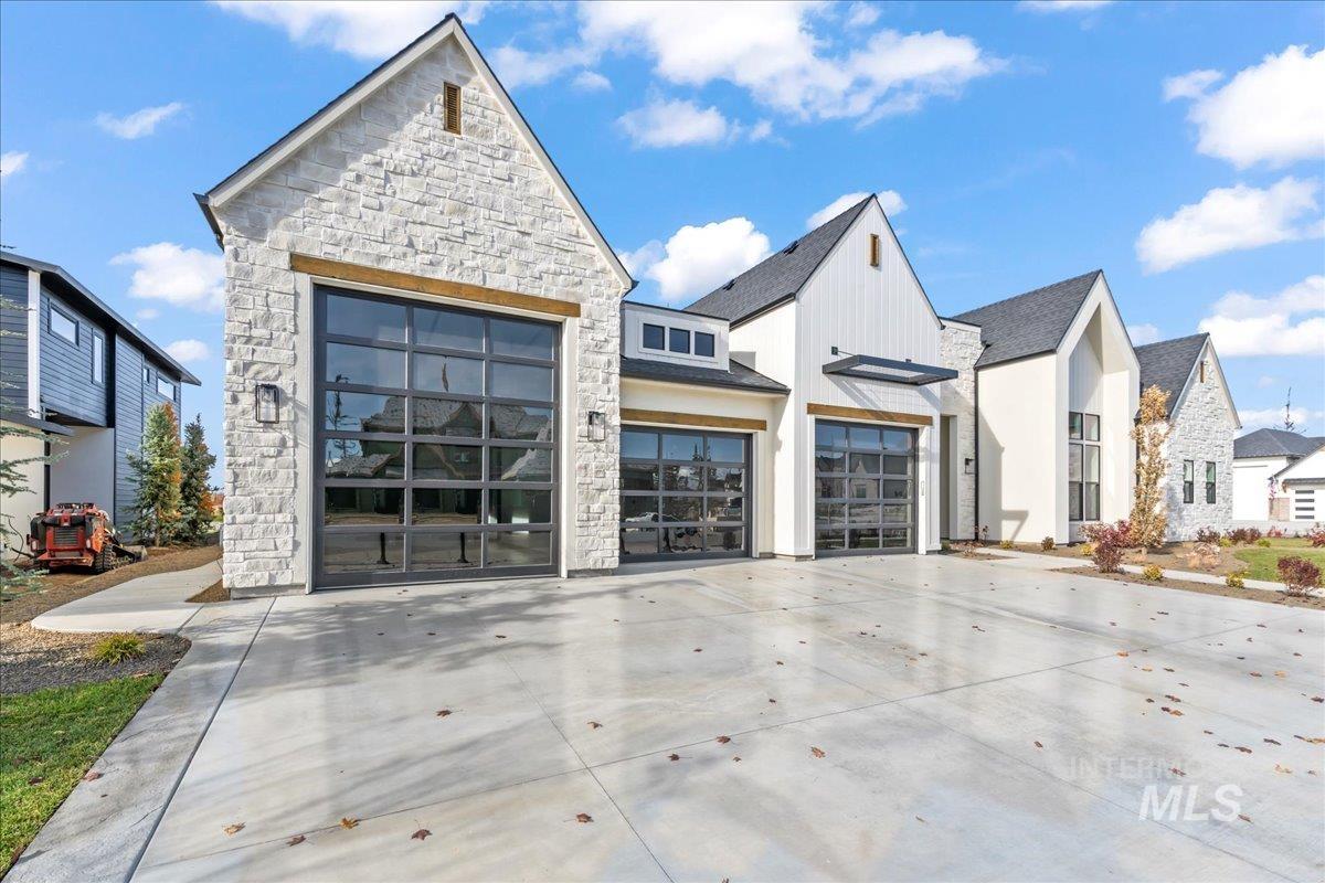 View of front of property with stone siding, concrete driveway, and roof with shingles