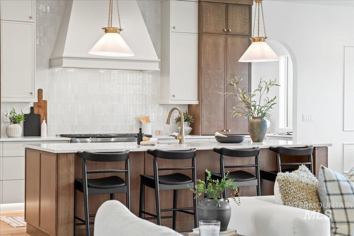 Kitchen with white cabinetry, custom range hood, decorative light fixtures, a breakfast bar, and decorative backsplash