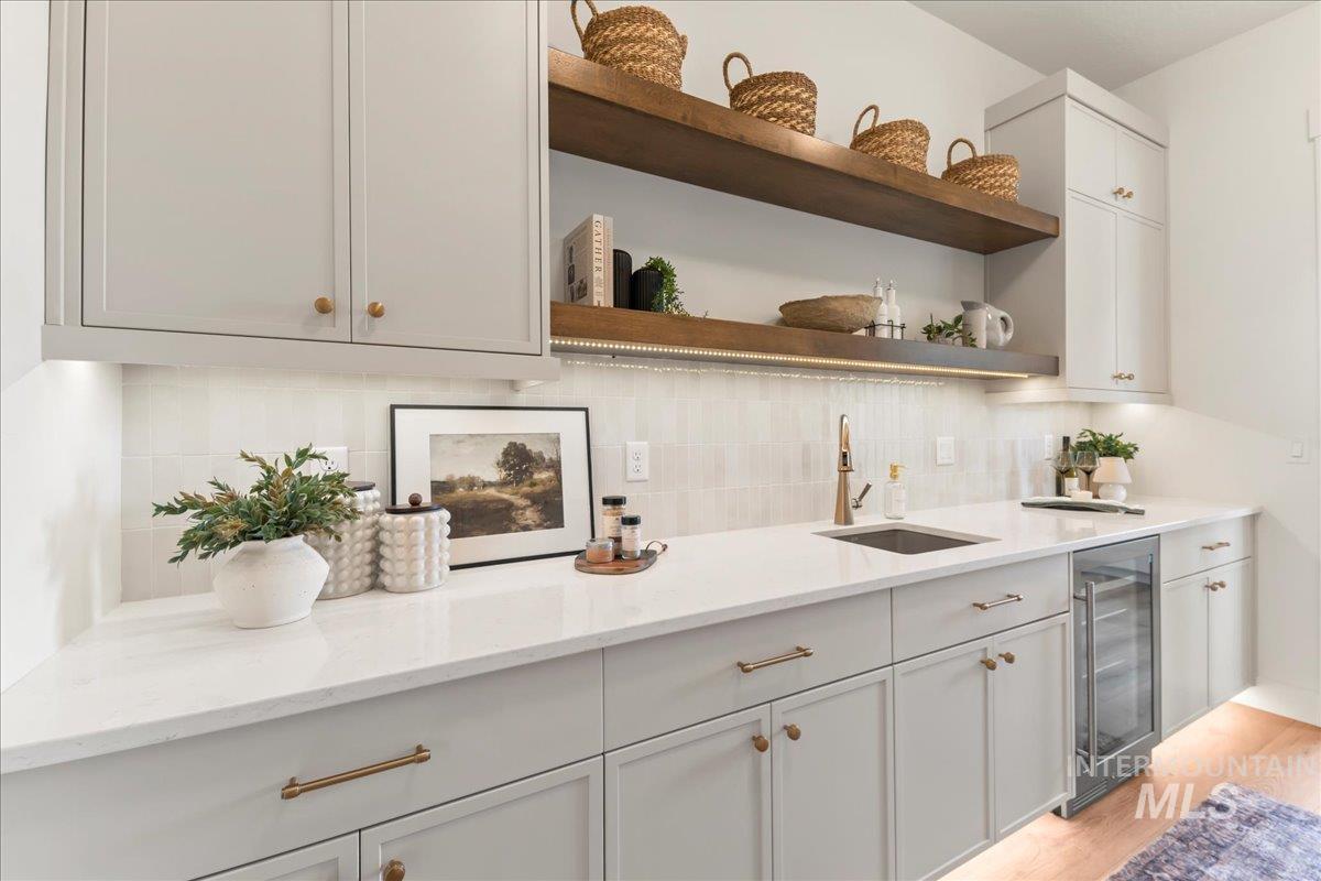 Bar area with tasteful backsplash, open shelves, wine cooler, light stone counters, and white cabinetry