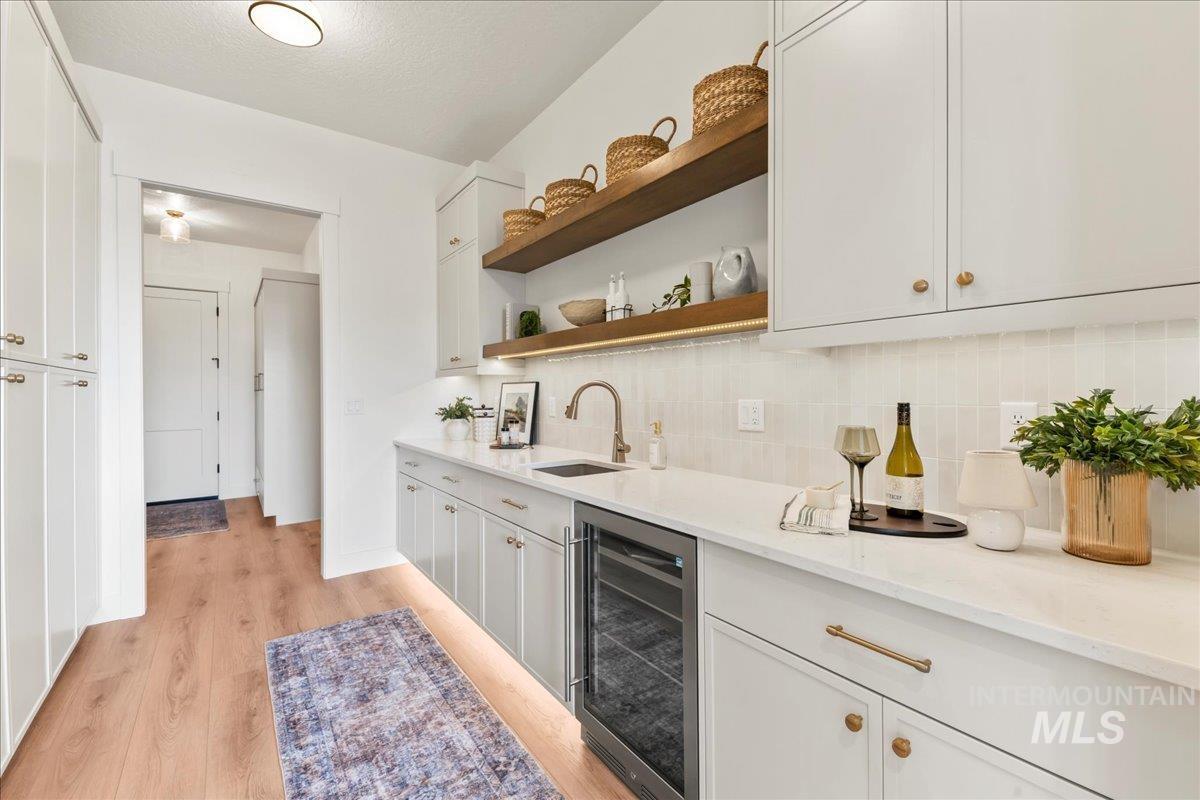 Bar featuring open shelves, wine cooler, light stone counters, decorative backsplash, and light wood-style flooring