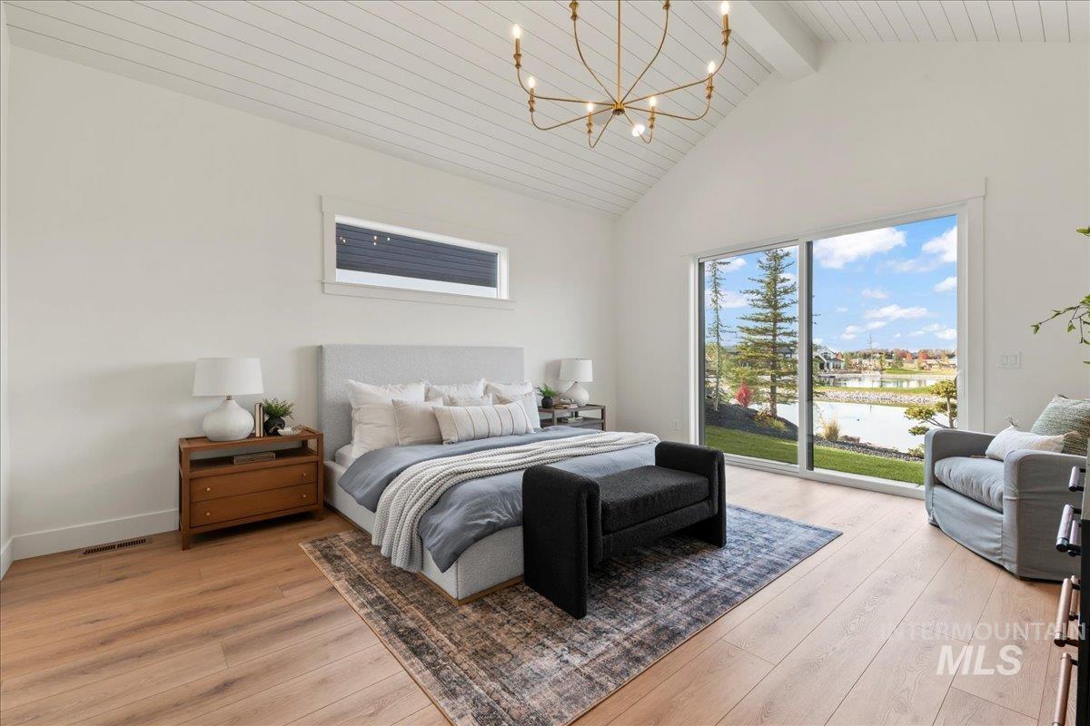 Bedroom with light wood-style flooring, access to outside, a water view, high vaulted ceiling, and a chandelier