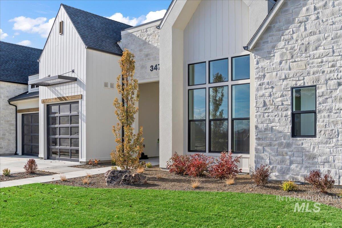View of property exterior featuring stone siding, board and batten siding, roof with shingles, a lawn, and driveway