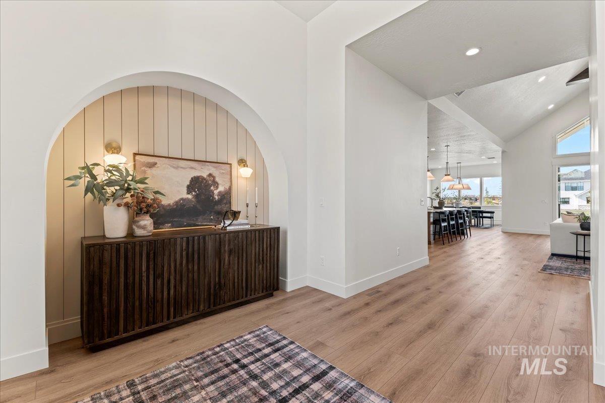 Corridor with arched walkways, light wood-style floors, high vaulted ceiling, and recessed lighting