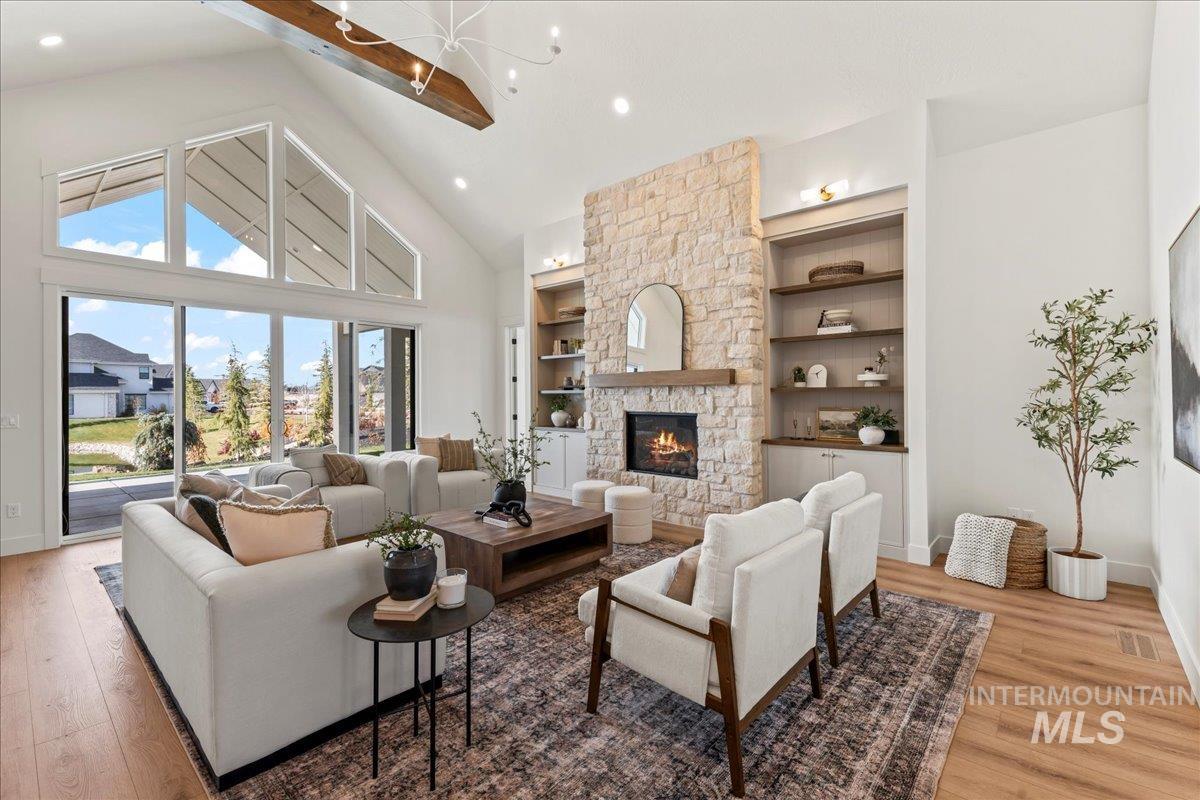 Living area with high vaulted ceiling, a stone fireplace, light wood-style flooring, beamed ceiling, and built in features