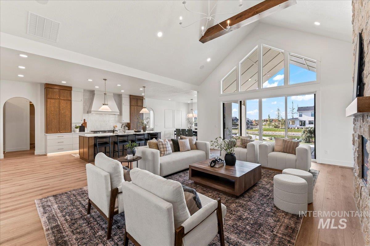 Living area with high vaulted ceiling, light wood finished floors, arched walkways, beamed ceiling, and a chandelier