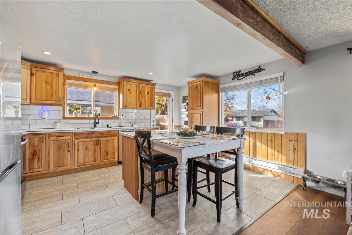 Kitchen with beam ceiling, backsplash, light wood-style floors, brown cabinets, and pendant lighting
