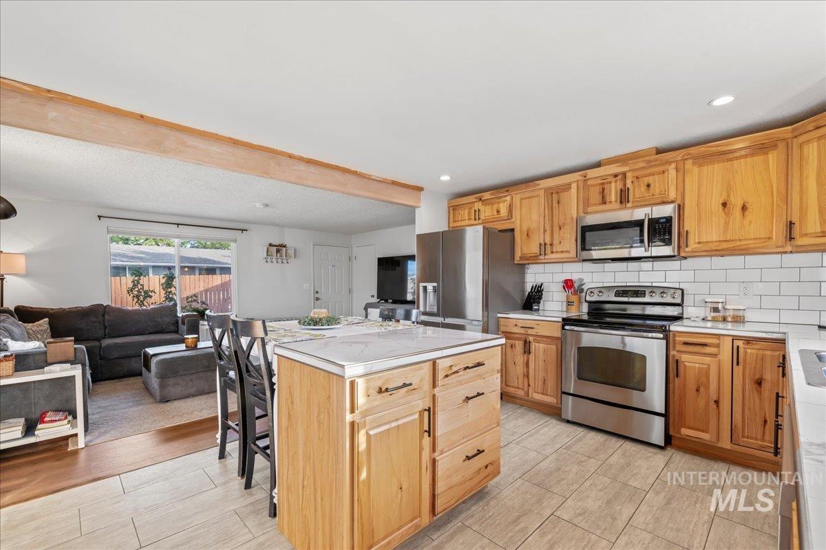 Kitchen with appliances with stainless steel finishes, decorative backsplash, a kitchen island, open floor plan, and light wood-style flooring