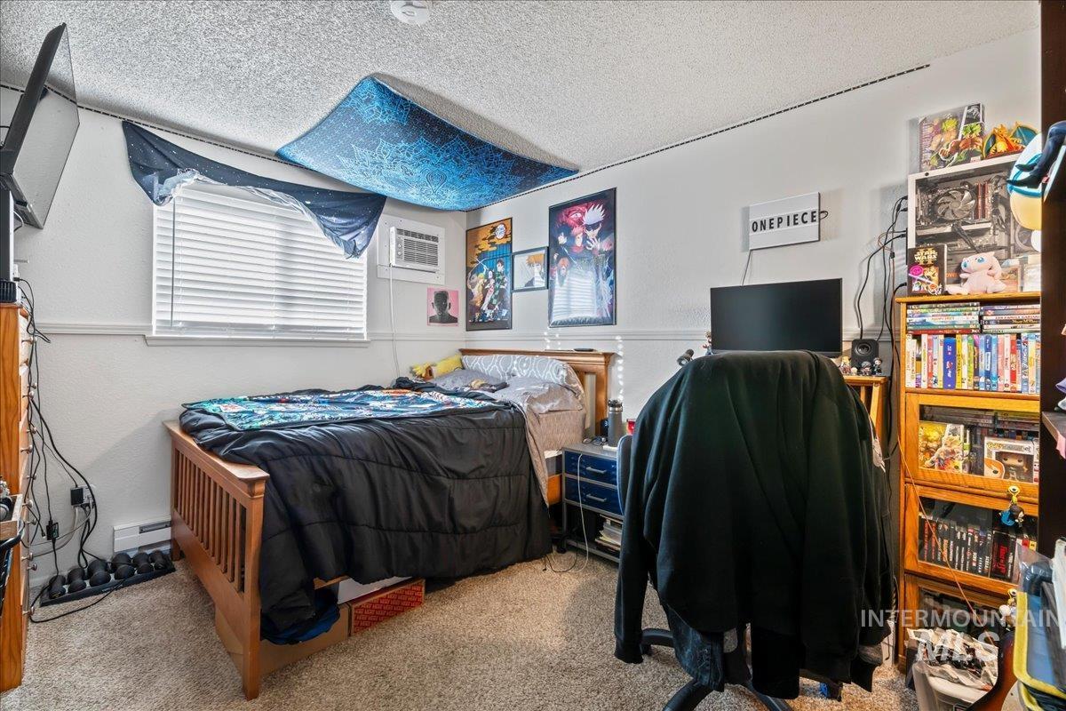 Carpeted bedroom featuring a textured ceiling, a wall unit AC, and a baseboard radiator
