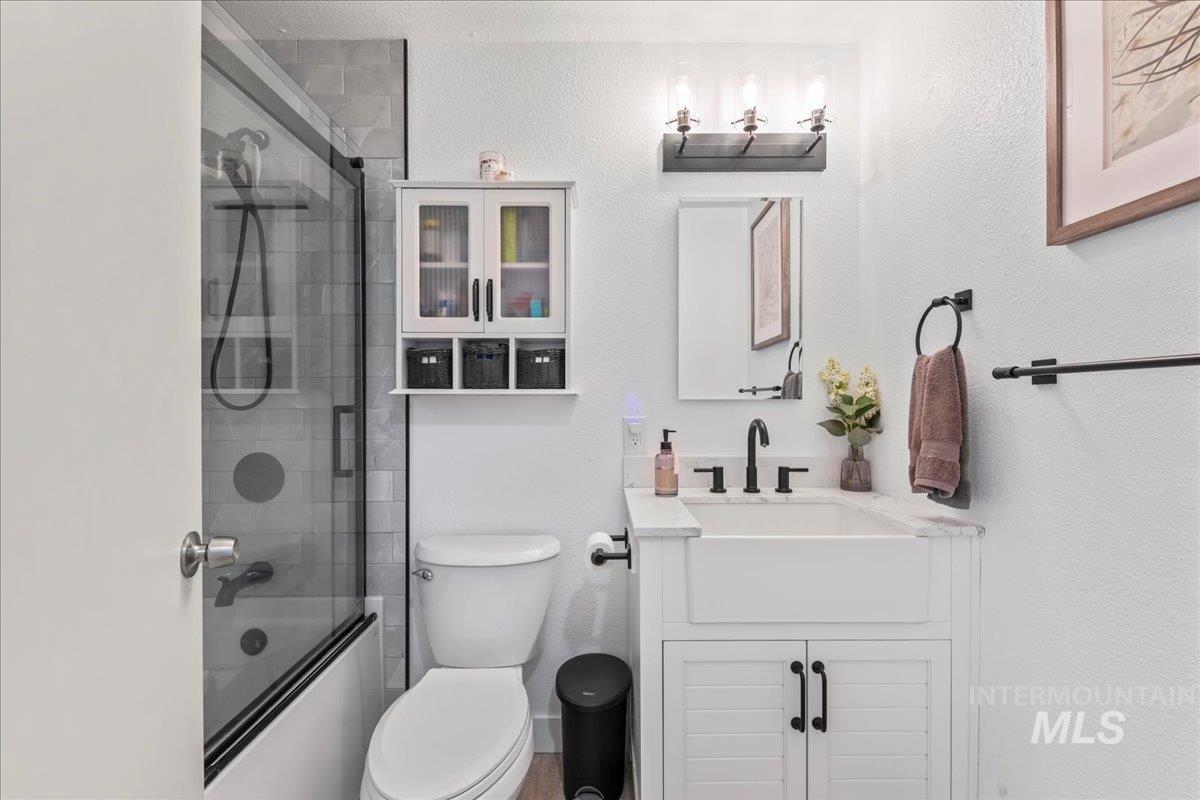 Full bathroom with vanity, a textured wall, and shower / bath combination with glass door