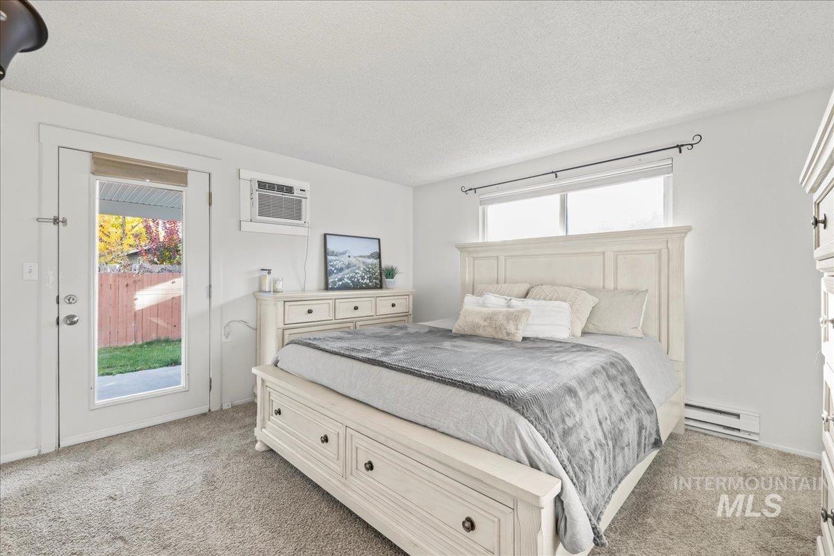 Bedroom featuring access to outside, baseboard heating, light carpet, multiple windows, and a textured ceiling