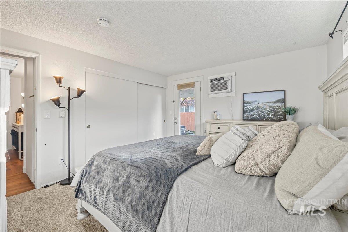 Carpeted bedroom with a closet, a textured ceiling, a wall mounted air conditioner, and access to outside