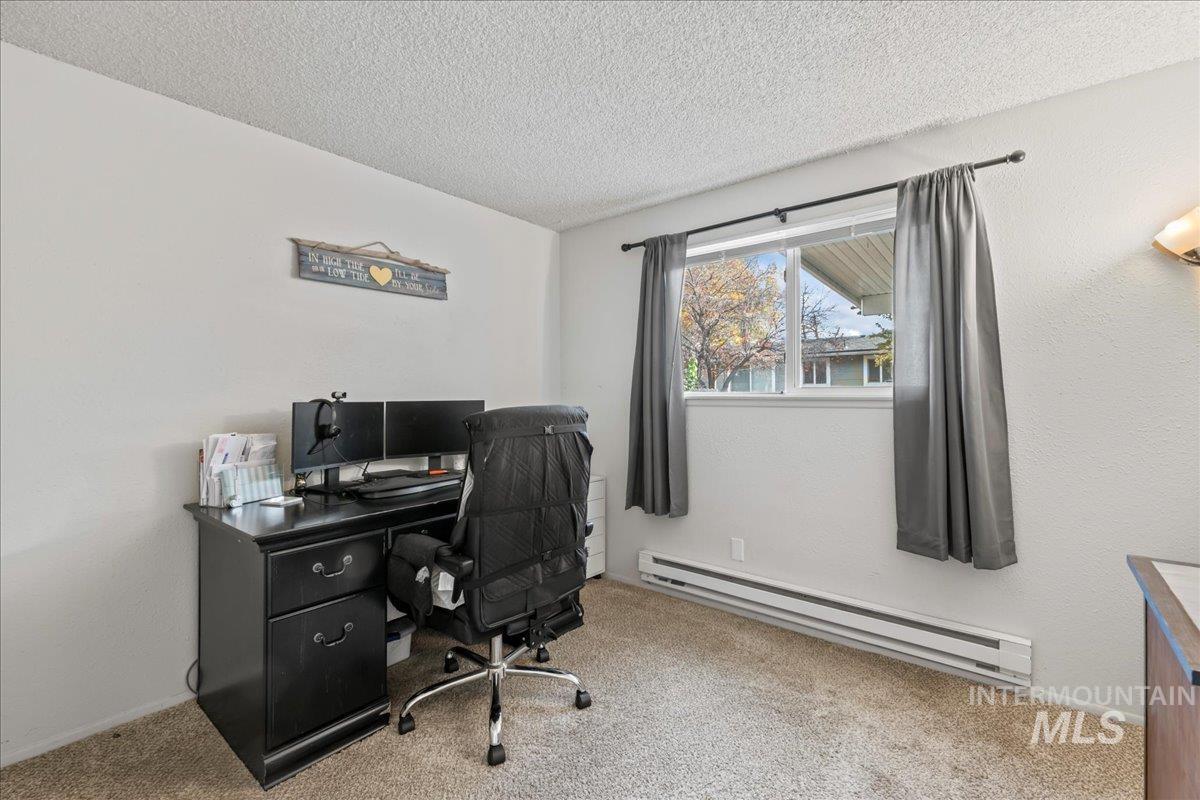 Office area with a baseboard heating unit, light carpet, a textured ceiling, and a textured wall