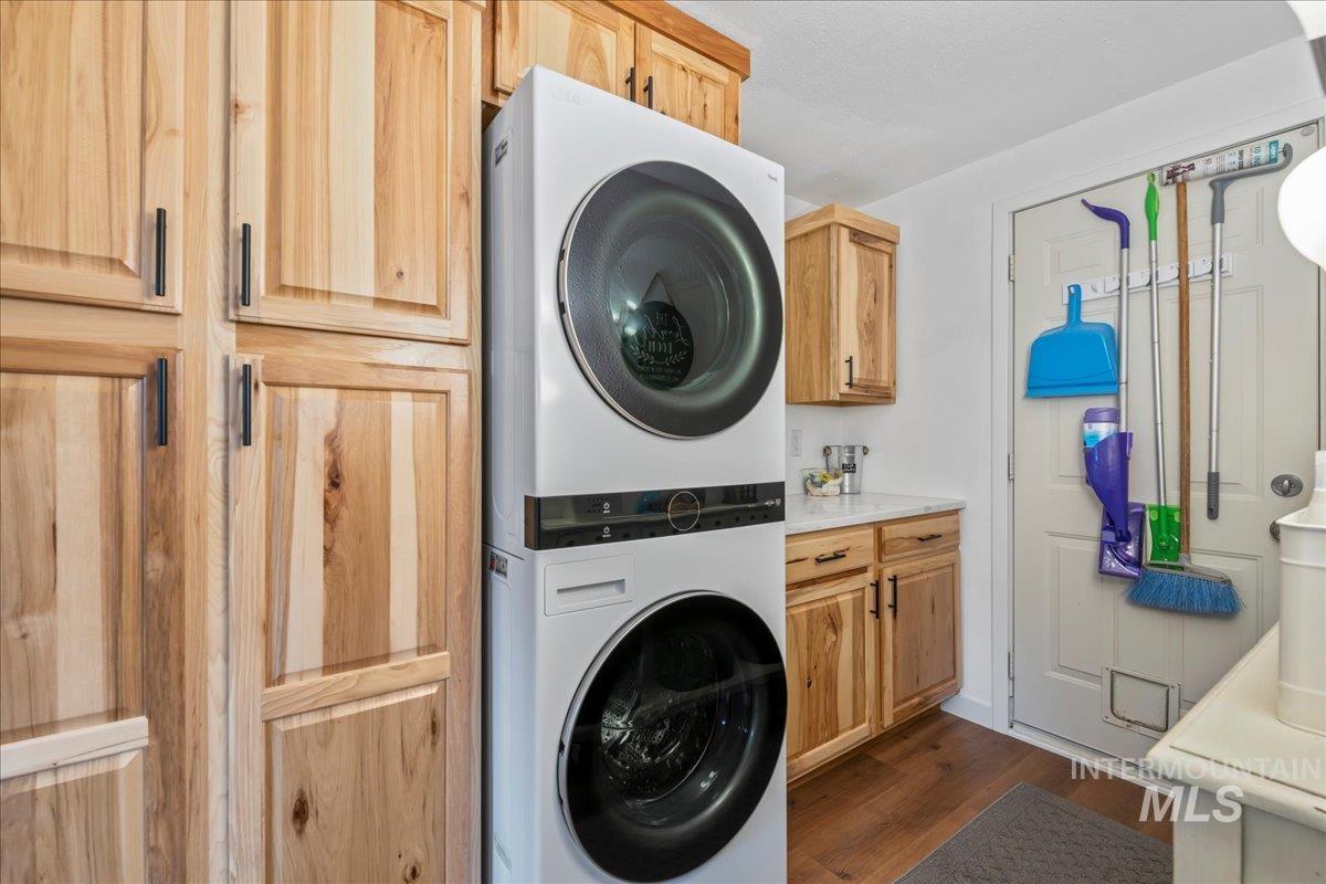 Laundry room with dark wood-style floors, stacked washer / dryer, and cabinet space