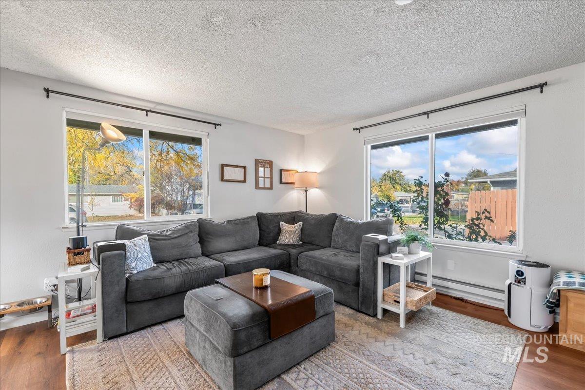 Living room with wood finished floors, a baseboard heating unit, and a textured ceiling