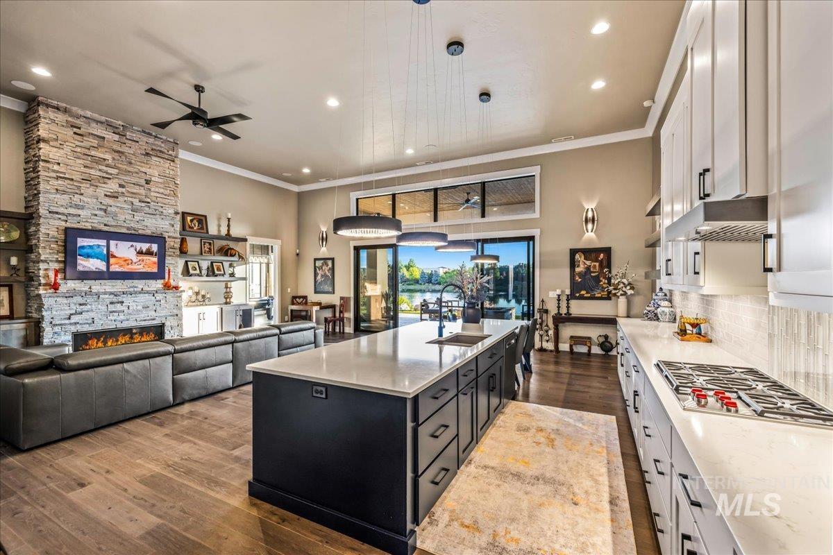 Kitchen featuring a ceiling fan, white cabinetry, a kitchen island with sink, wood finished floors, and stainless steel gas stovetop