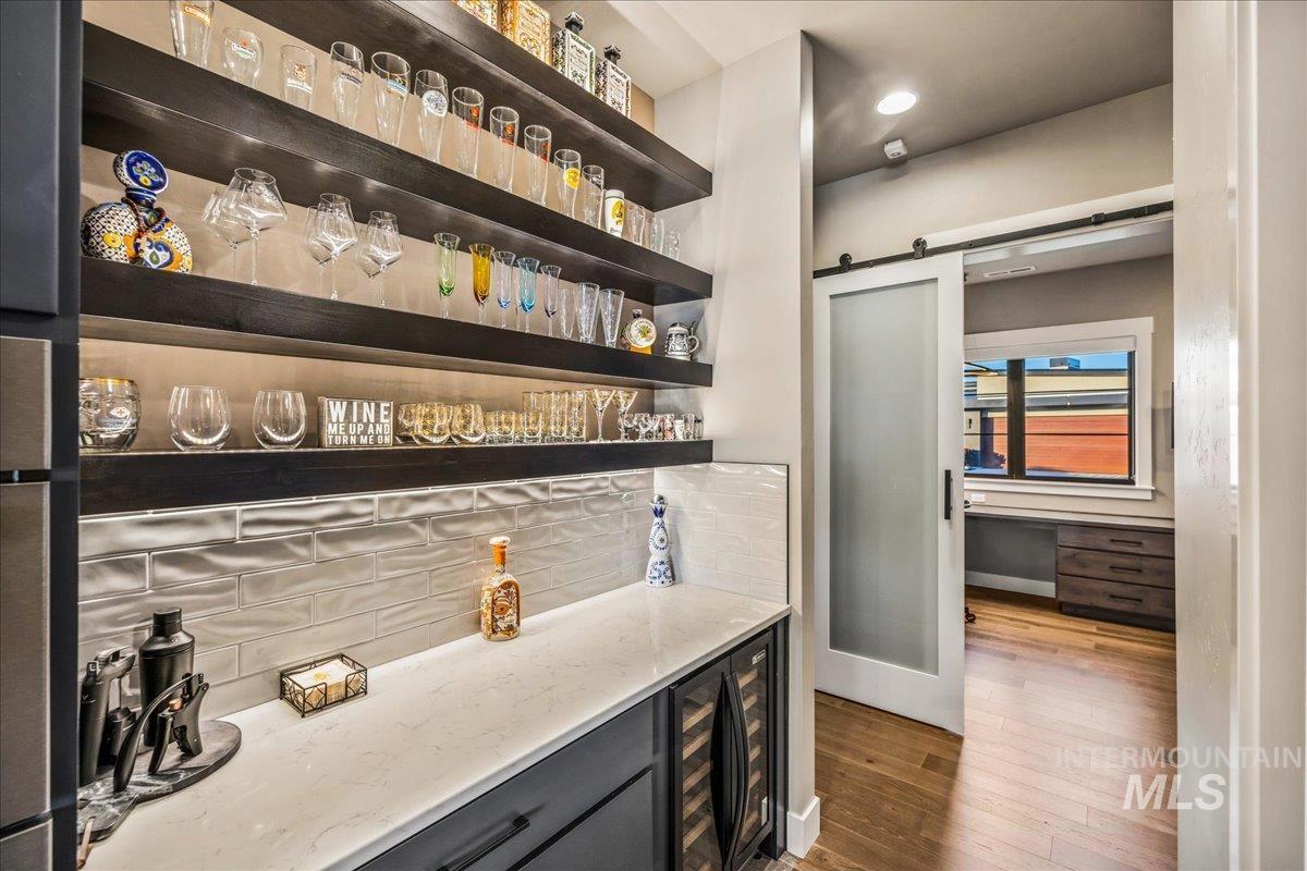 Indoor dry bar featuring tasteful backsplash, beverage cooler, a barn door, wood finished floors, and wall oven