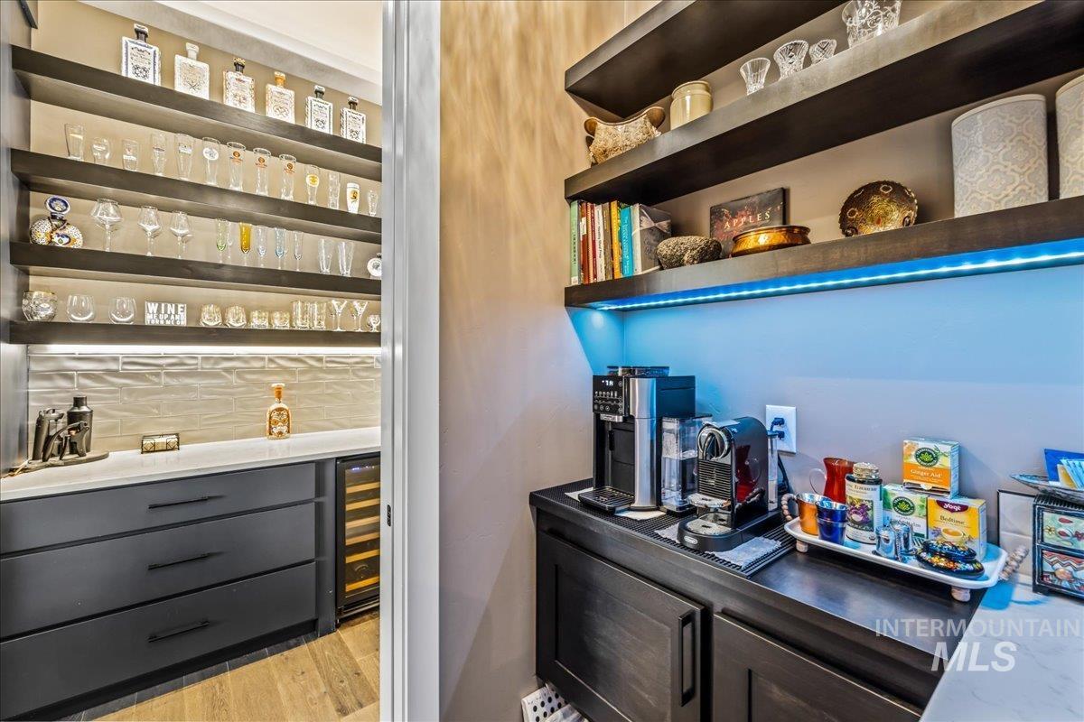 Indoor dry bar featuring gray cabinetry, tasteful backsplash, wine cooler, light stone counters, and light wood-style floors