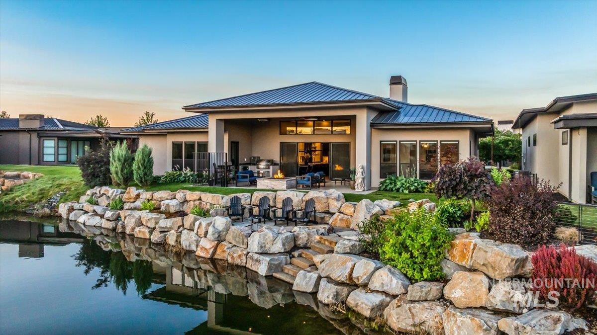 Back of property at dusk with a standing seam roof, a metal roof, a chimney, stucco siding, and a patio area