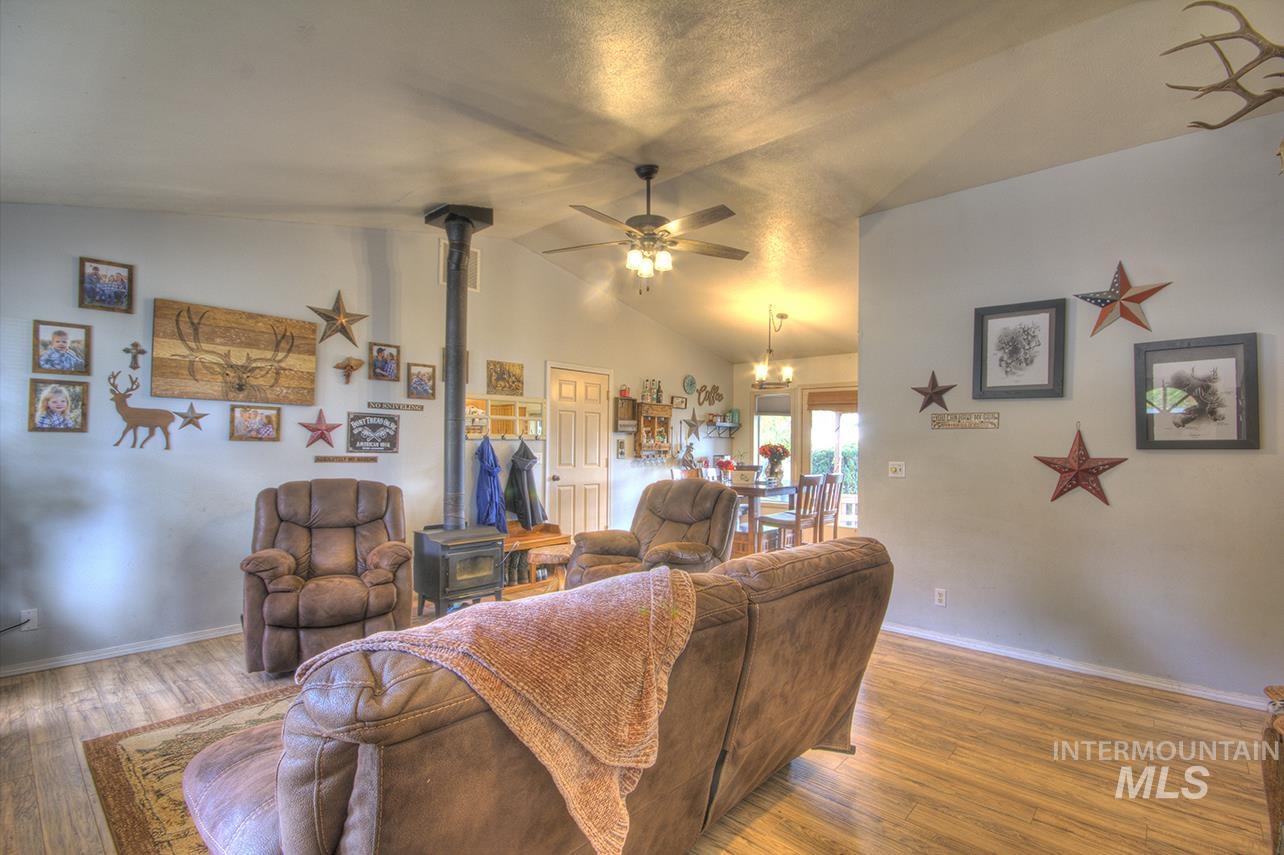 Living area with a wood stove, wood finished floors, vaulted ceiling, a ceiling fan, and a chandelier