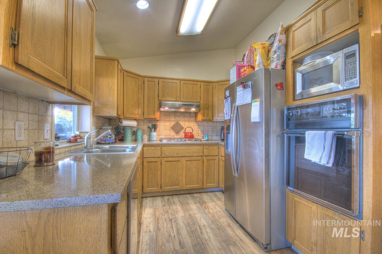 Kitchen featuring appliances with stainless steel finishes, light wood finished floors, backsplash, brown cabinets, and vaulted ceiling