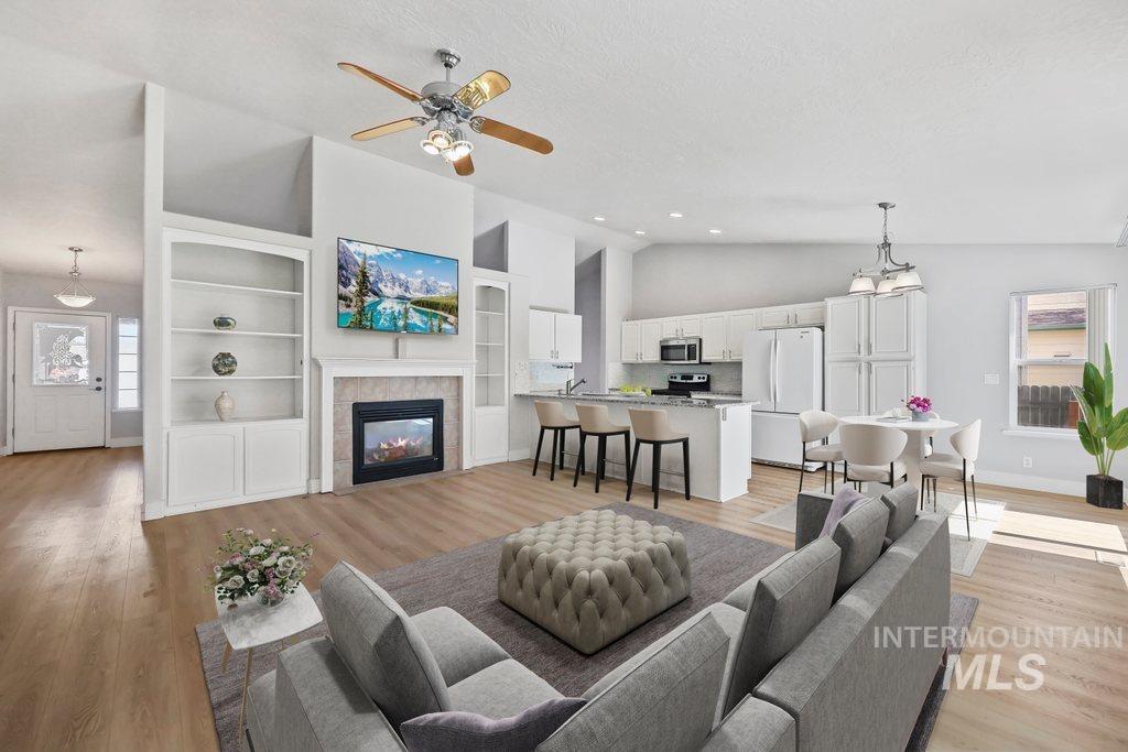 Living room featuring vaulted ceiling, light wood-type flooring, ceiling fan, a tile fireplace, and a textured ceiling