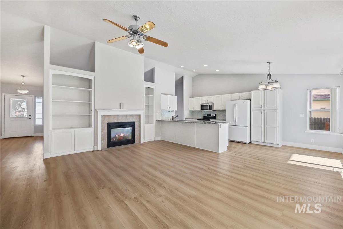 Unfurnished living room featuring light wood-style flooring, a tiled fireplace, a ceiling fan, and high vaulted ceiling