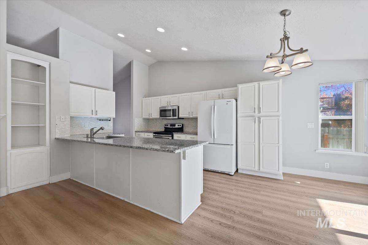 Kitchen featuring backsplash, stainless steel appliances, a peninsula, white cabinets, and dark stone countertops