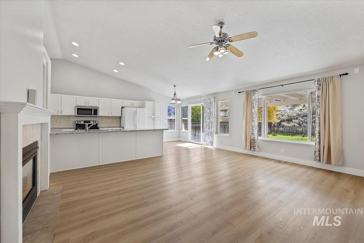 Unfurnished living room with light wood finished floors, ceiling fan, a tiled fireplace, recessed lighting, and lofted ceiling