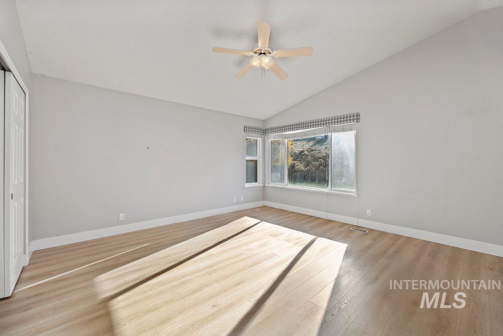 Empty room with lofted ceiling, light wood finished floors, and ceiling fan
